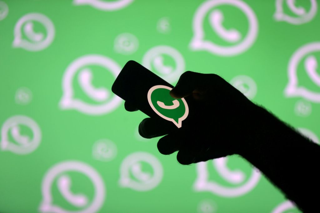Seorang pria berpose dengan ponsel pintar di depan logo Whatsapp yang ditampilkan dalam ilustrasi ini.