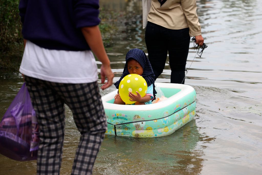 Warga menarik perahu karet mainan bersama anaknya saat melintasi banjir yang masih menggenang selama tiga bulan di Desa Kasiyan, Kecamatan Sukolilo, Kabupaten Pati, Jawa Tengah, Kamis (16/3/2023).