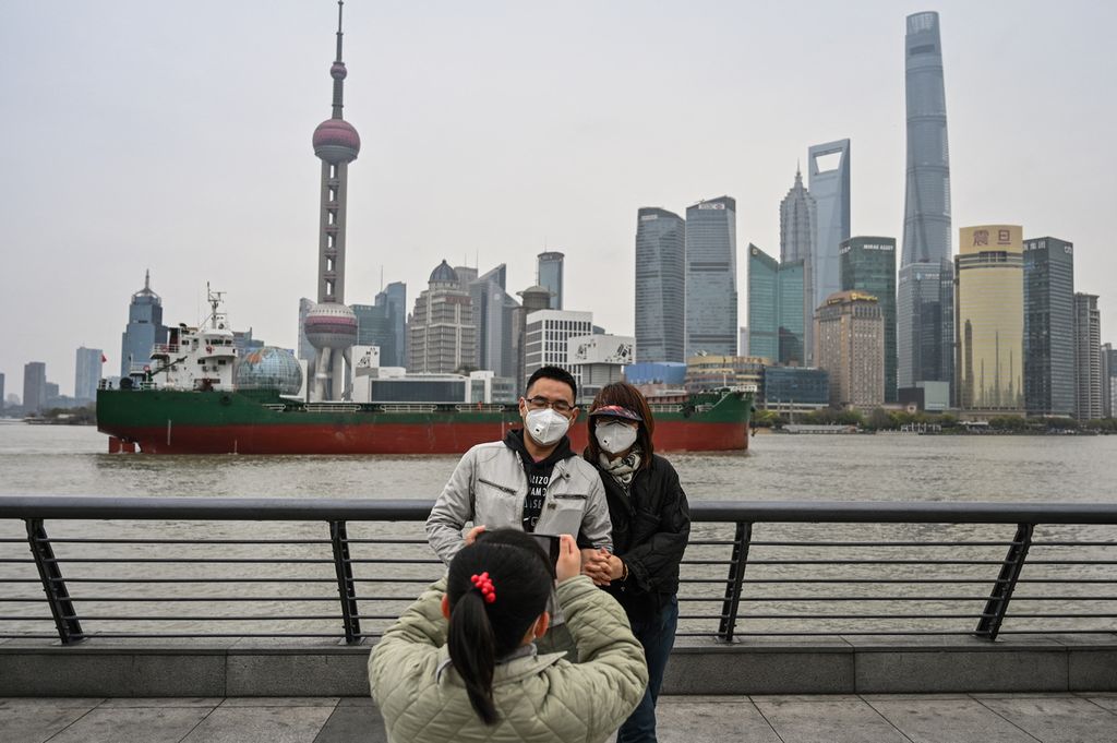 Seorang anak perempuan memotret pasangan wisatawan di tepi Sungai Huangpu, Puxi , China, yang mengalami penguncian wilayah mulai Jumat (1/4/2022). Di latar belakang tampak distrik finansial Pudong yang juga tengah mengalami penguncian wilayah.  