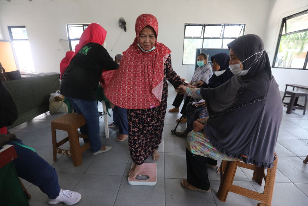 Kader posyandu mengukur berat badan warga lansia di Balai RT 012 RW 007, Kelurahan Pondok Kelapa, Jakarta Timur, Kamis (14/7/2022).