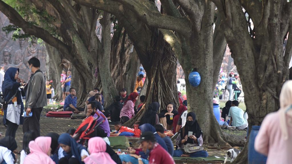 Warga memanfaatkan kerindangan pohon peneduh jalan untuk beristirahat saat berkunjung ke Taman Mini Indonesia Indah (TMII), Jakarta Timur, Minggu (2/8/2020). TMII menjadi salah satu tempat wisata yang banyak dikunjungi warga untuk mengisi libur Lebaran.