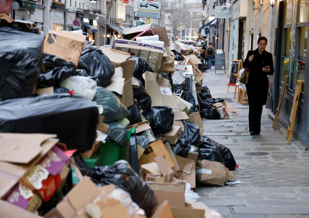 Seorang perempuan berjalan di samping tumpukan kantong berisi sampah yang dibiarkan teronggok di pinggir jalan setelah para pekerja sampah berunjuk rasa menentang kebijakan pensiun Pemerintah Perancis, Senin (20/3/2023). 