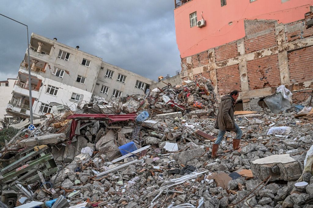 Wytekin Mumoglu (46), Selasa (21/2/2023), berjalan di atas reruntuhan rumahnya yang roboh akibat gempa di kota Samandag, Turki. Proses rehab rekon di wilayah terdampak gempa segera dimulai. 