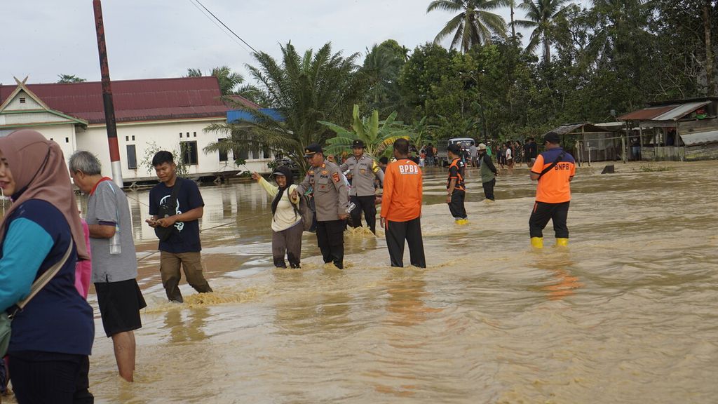 Warga dibantu petugas melintasi jalan yang tergenang banjir di Kelurahan Sepaku, Kecamatan Sepaku, Penajam Paser Utara, Kalimantan Timur, Jumat (17/3/2023). Menurut penuturan warga, banjir di dekat proyek IKN ini merupakan yang terparah setelah tahun 2019.
