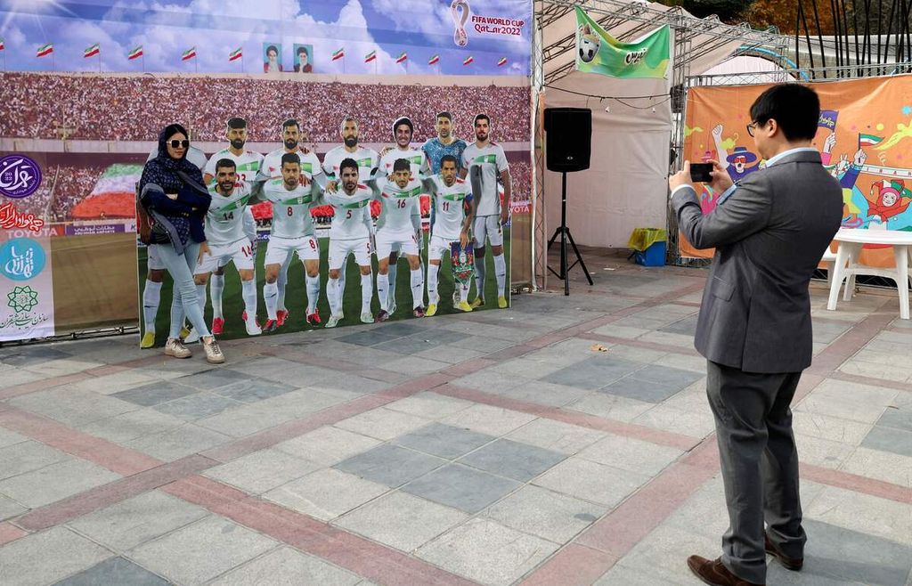 Seorang perempuan Iran berfoto dengan latar belakang gambar tim nasional Iran di taman bertema sepak bola untuk menyambut Piala Dunia Qatar 2022 di depan Mellat Park, Teheran, Iran, Jumat (28/11/2022). 