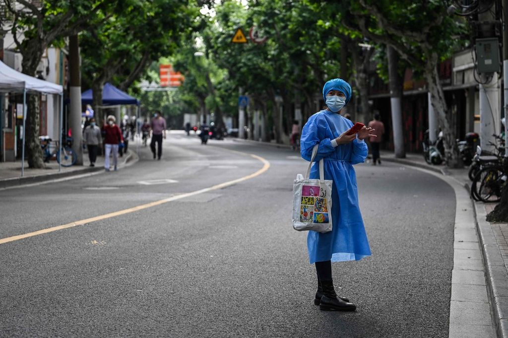 Seorang perempuan, dengan memakai baju pelindung khusus, berdiri di pinggir salah satu ruas jalan di Distrik Jing'an yang tengah diberlakukan penguncian wilayah (<i>lockdown</i>) di Shanghai, China, Rabu (25/5/2022).