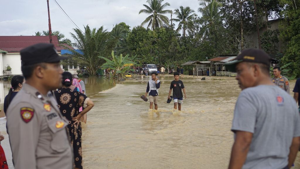Warga dibantu petugas melintasi jalan yang tergenang banjir di Kelurahan Sepaku, Kecamatan Sepaku, Penajam Paser Utara, Kalimantan Timur, Jumat (17/3/2023). Menurut penuturan warga, banjir di dekat proyek IKN ini merupakan yang terparah setelah tahun 2019.