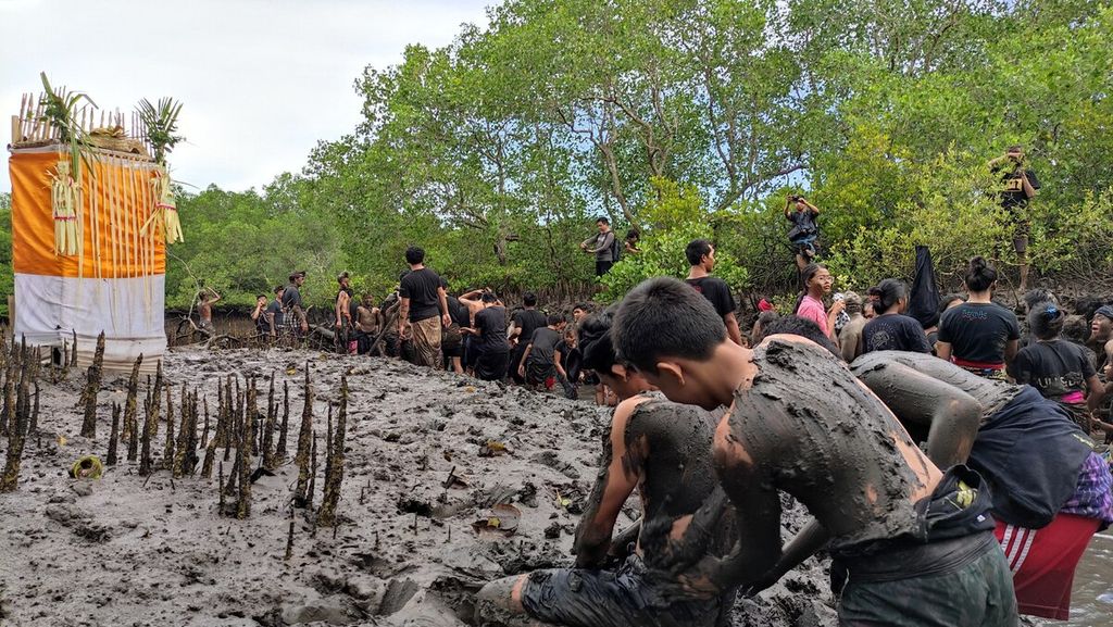 <i>Krama</i> (warga) dan <i>yowana </i>(pemuda dan pemudi) Desa Adat Kedonganan, Kedonganan, Kuta, Kabupaten Badung, saling membalurkan lumpur hutan bakau ketika mengikuti tradisi <i>mabuug-buugan </i>di tengah hutan mangrove Taman Hutan Raya Ngurah Rai, Kamis (23/3/2023).