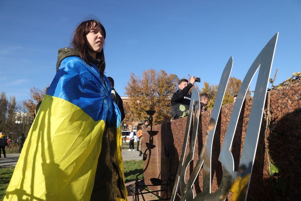 Seorang gadis menyelimuti tubuhnya dengan bendera Ukraina, menyiratkan kegembiraannya setelah kota Kherson berhasil diambil alih oleh militer Ukraina, SEnin (14/11/2022). 