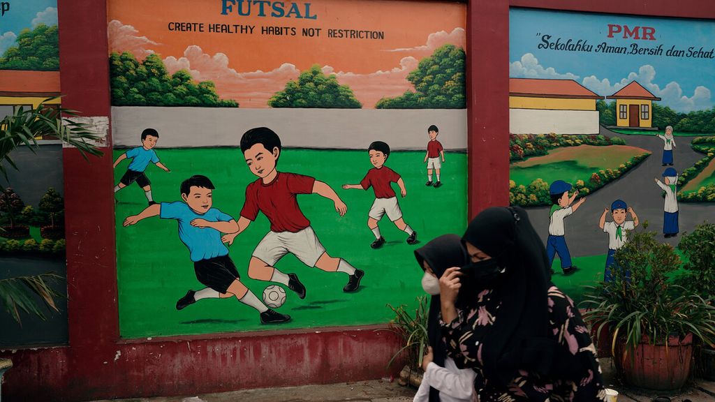 Warga melintasi mural olahraga anak yang menghiasi sebuah gedung sekolah dasar di Sukapura, Cilincing, Jakarta Utara, Senin (14/3/2022).