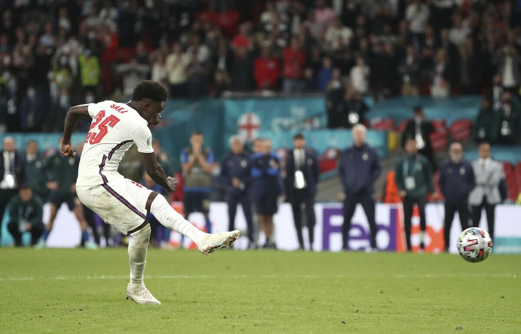Pemain timnas Inggris, Bukayo Saka, melepas tendangan penalti yang gagal berbuah gol pada adu penalti dalam laga final Piala Eropa melawan Italia di Stadion Wembley, London, Minggu (11/7/2021). Kegagalan Saka membuat Inggris kalah dari Italia dan Saka menjadi sasaran penghinaan di media sosial. 