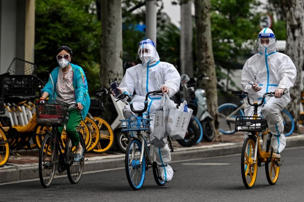 Para pekerja yang mengenakan alat pelindung diri bersepeda di sebuah ruas jalan selama penguncian Covid-19 di distrik Jing'an, Shanghai, Minggu (29/5/2022).