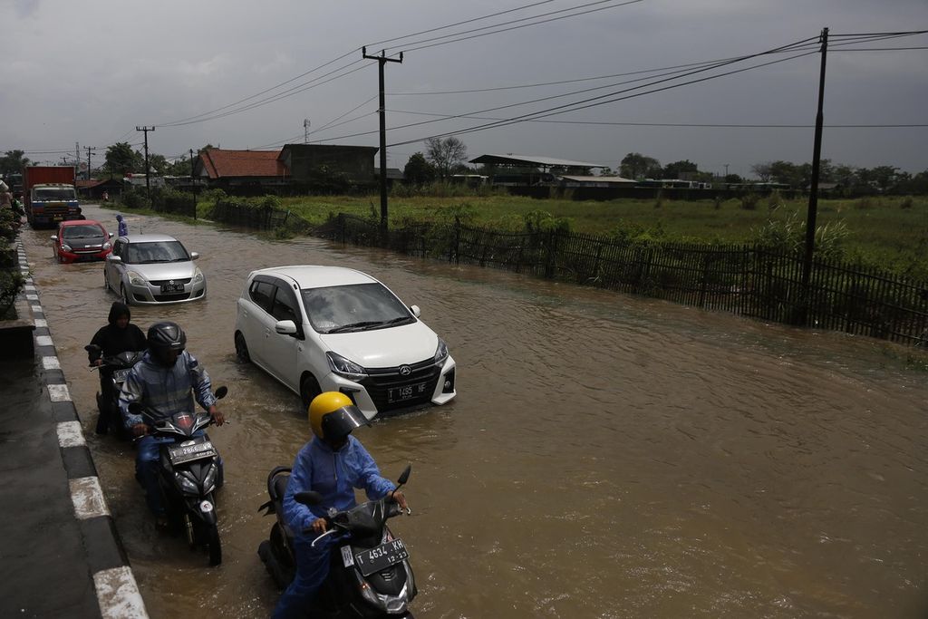 Pengendara berusaha melintasi banjir yang menggenangi Jalan Pantura di kawasan Kota Baru, Karawang, Jawa Barat, Senin (27/2/2023). Kondisi jalan yang rendah ditambah meluapnya anak kali di kawasan itu menyebabkan jalan tersebut menjadi langganan banjir.