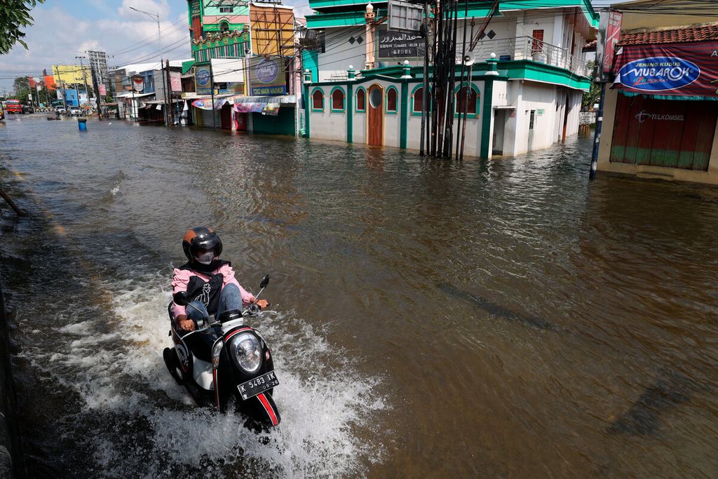 Pengemudi motor melintasi banjir dengan latar belakang kawasan pertokoan oleh-oleh yang tutup di Tanggulangin, Desa Jati Wetan, kecamatan Jati, Kabupaten Kudus, Jawa Tengah, Rabu (4/1/2023).