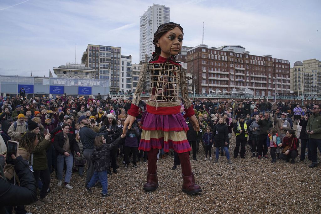 Boneka raksasa Si Amal Kecil, yang merepresentasi sosok perempuan pengungsi Suriah berusia 10 tahun, memimpin aksi jalan kaki pada senja hari di Pantai Brighton, Inggris, 30 Maret 2023, sebagai upaya menebar pesan tentang harapan dan solidaritas kepada para pengungsi di mana pun mereka berada. 