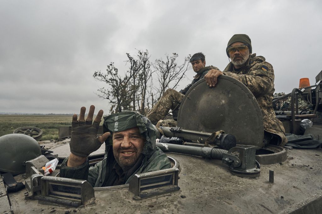 Tentara Ukraina tersenyum di dalam kendaraan militer yang melaju di jalan yang telah direbut kembali oleh pasukan Ukraina di wilayah Kharkiv, Ukraina, Senin (12/9/2022). 