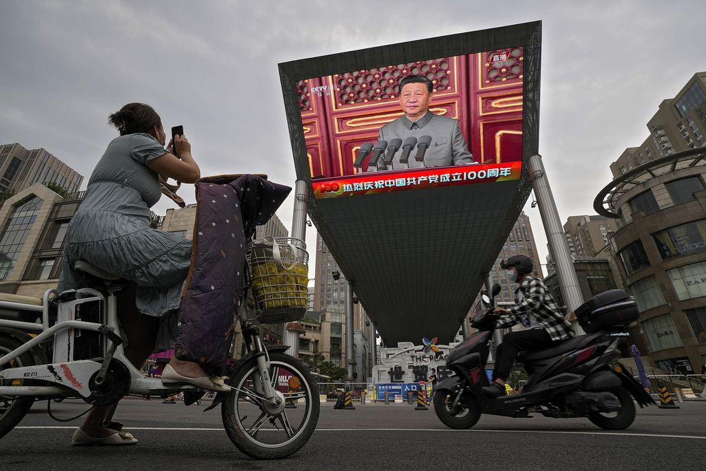 Seorang perempuan di atas sepeda motor listriknya mengambil gambar layar televisi besar di luar sebuah pusat perbelanjaan yang menampilkan Presiden China Xi Jinping di tengah perayaan 100 tahun Partai Komunis China di Lapangan Tiananmen, Beijing, China, 1 Juli 2021. 