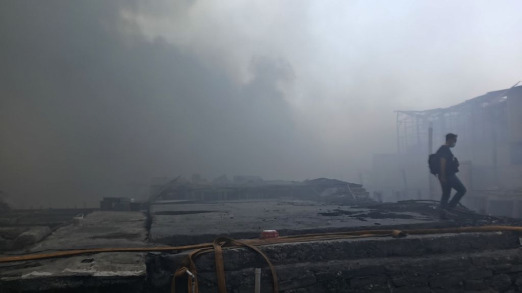 A resident carried goods and passed through the debris and thick black smoke that enveloped the settlement of residents in RW 003, Jalan Kapuk Utara 2, Kapuk Muara, Penjaringan, North Jakarta, on Sunday (30/7/2023) afternoon.