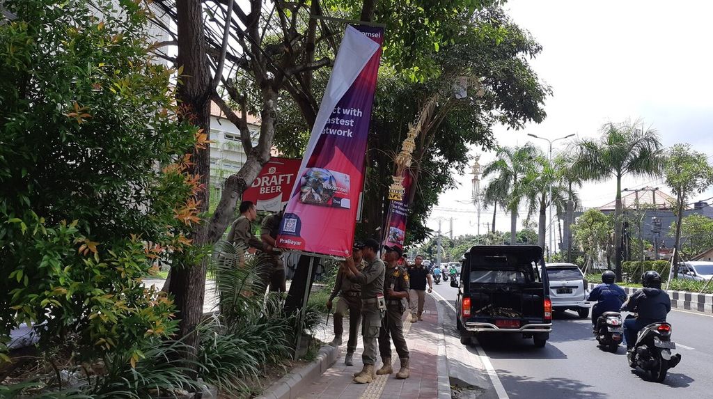 Petugas Satpol PP Bali, Jumat (11/11/2022), menurunkan spanduk yang terpasang di tepi Jalan Bypass Ngurah Rai, Badung, Bali, dalam rangka persiapan menyambut KTT G20 di Bali.