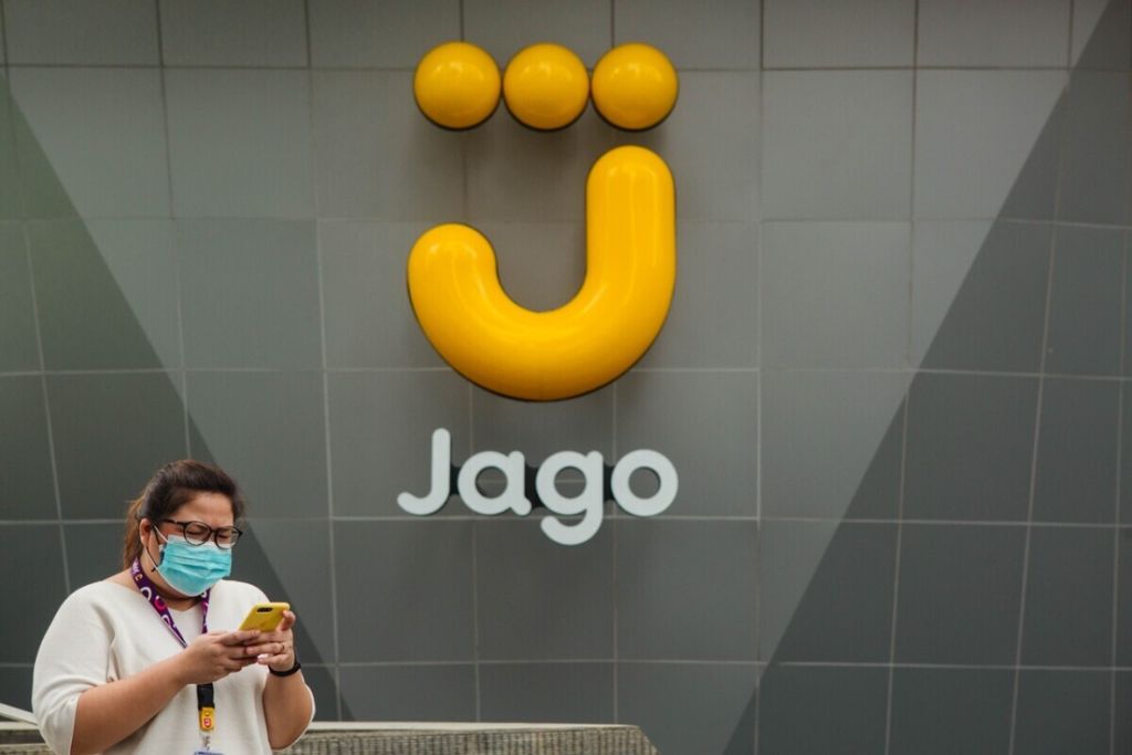 Seorang warga sedang berjalan melewati logo Bank Jago.