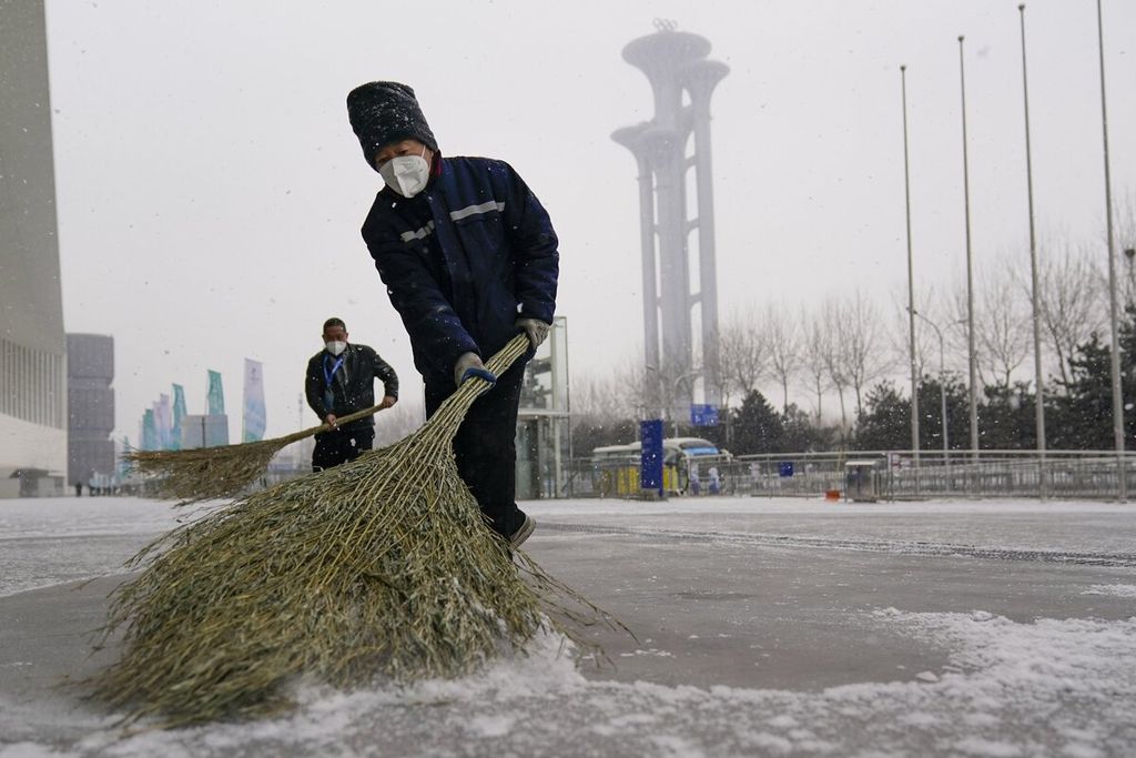 Pekerja membersihkan salju dari trotoar di luar media center Olimpiade Musim Dingin 2022 di Beijing, China (20/1/2022). Penyelenggaraan Olimpiade yang memakai salju buatan dikritik karena menghabiskan 185 juta liter air.