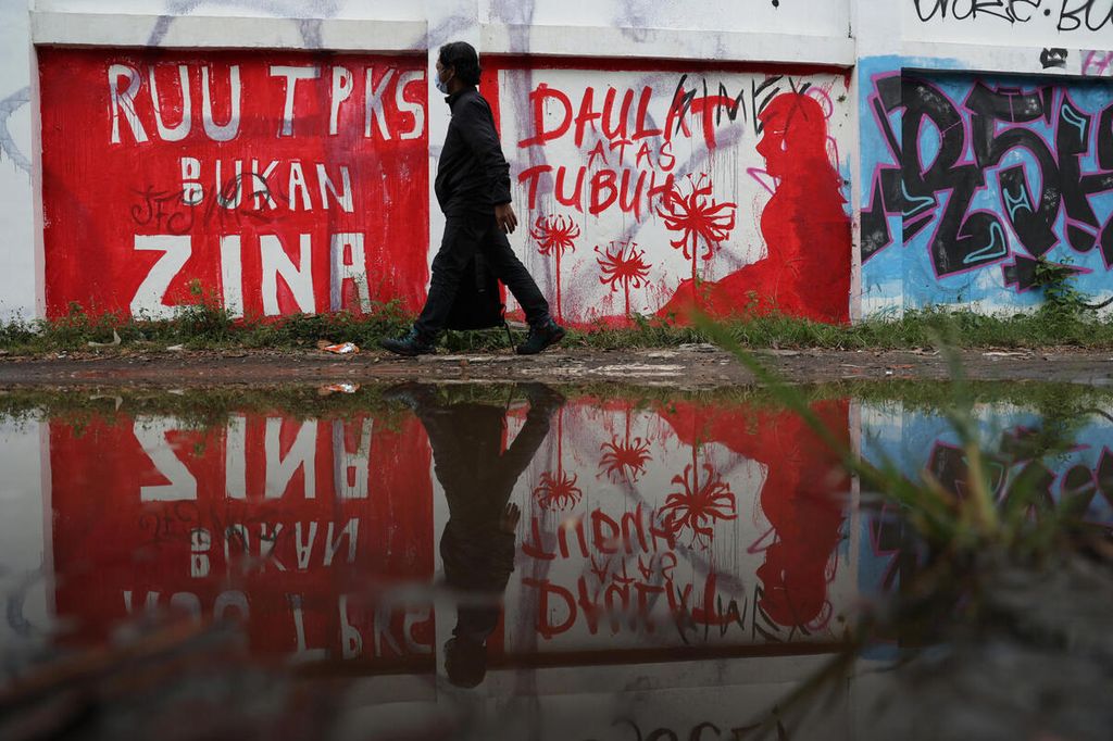 Warga melintas di depan mural berisi seruan untuk mendorong pengesahan Rancangan Undang-undang Tindak Pidana Kekerasan Seksual yang dibuat di tembok Stadion Kridosono, Yogyakarta, Senin (10/1/2021).