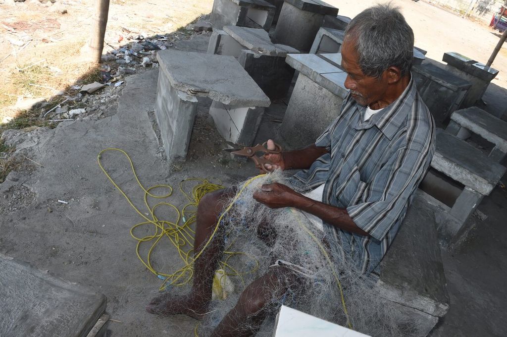 Asmali memperbaiki jaringnya yang rusak di Pantai Tambak Wedi, Kota Surabaya, Jawa Timur, Senin (29/8/2022). Sebagian besar nelayan setempat membeli pertalite sebagai bahan bakar mesin perahunya secara eceran. Untuk 1 liter pertalite, mereka beli seharga Rp 10.000. Dalam sehari, nelayan menghabiskan 3-5 liter pertalite.