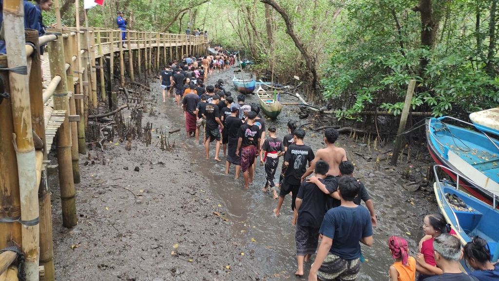 <i>Krama </i>(warga) dan <i>yowana </i>(pemuda dan pemudi) Desa Adat Kedonganan, Kedonganan, Kuta, Kabupaten Badung, menyusuri sungai di tengah hutan bakau untuk mengikuti tradisi <i>mabuug-buugan </i>di tengah Taman Hutan Raya Ngurah Rai, Kamis (23/3/2023).