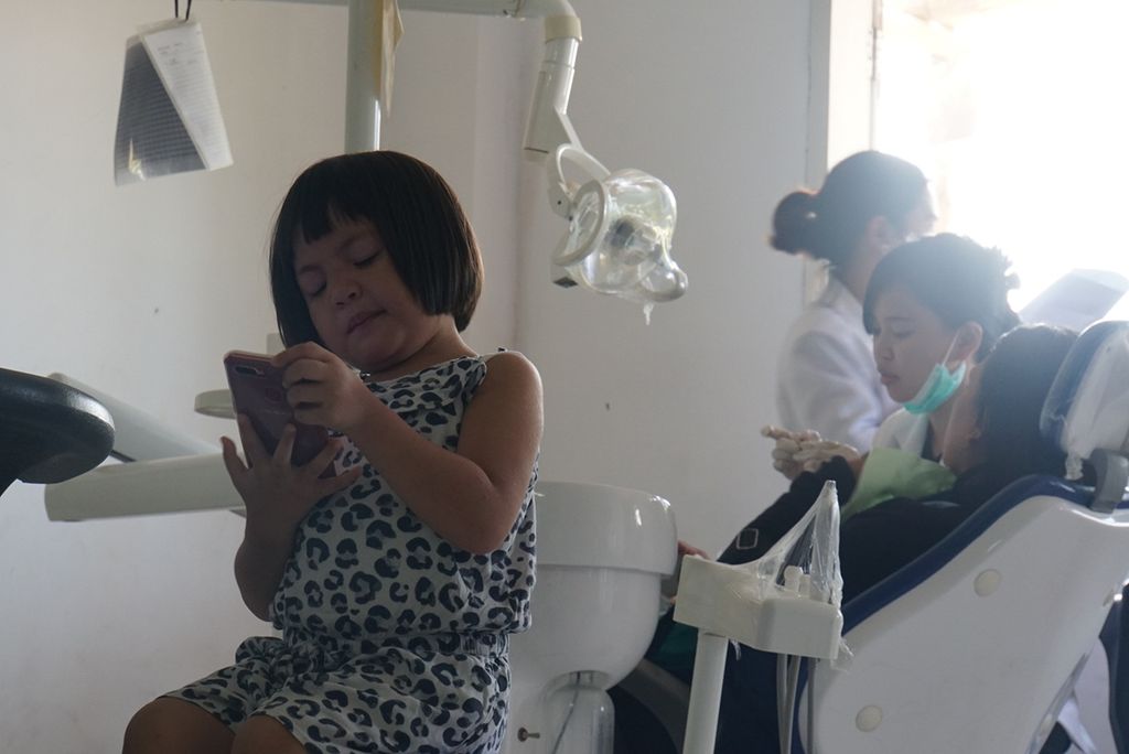 Seorang anak bermain ponsel selagi menunggu ibunya menerima perawatan gigi di Rumah Sakit Gigi dan Mulut Universitas Sam Ratulangi Manado, Sulawesi Utara, Jumat (6/12/2019).