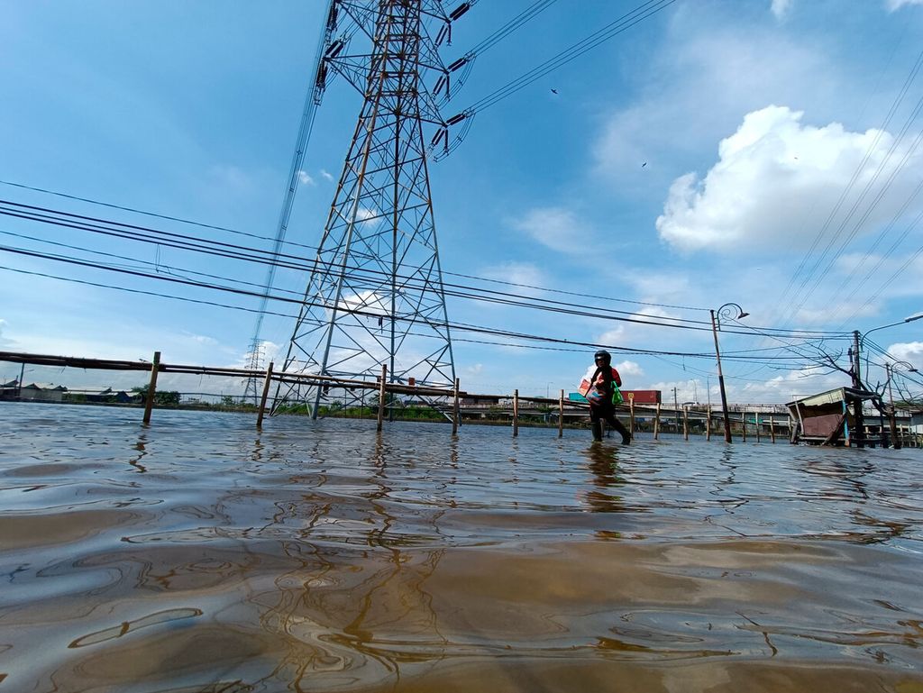 Warga melintasi pasang air laut yang menggenangi akses jalan di Kampung Tambakmulyo, Kota Semarang, Jawa Tengah. Jumat (20/5/2022). Dalam waktu beberapa tahun ini, ketinggian dan luasan area banjir semakin meluas karena banyak faktor, antara lain, penurunan permukaan tanah, abrasi, hingga perubahan iklim. 
