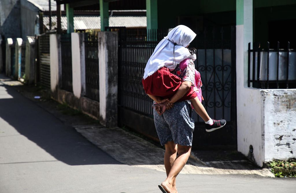 Ibu Nurjanah berjalan kaki sambil menggendong putrinya Sabrina yang sakit saat pulang sekolah dari SD Negeri Pondok Betung 02, Pondok Aren, Tangerang Selatan, Banten, menuju kediamannya yang berjarak sekitar dua kilometer, Senin (24/1/2022). 