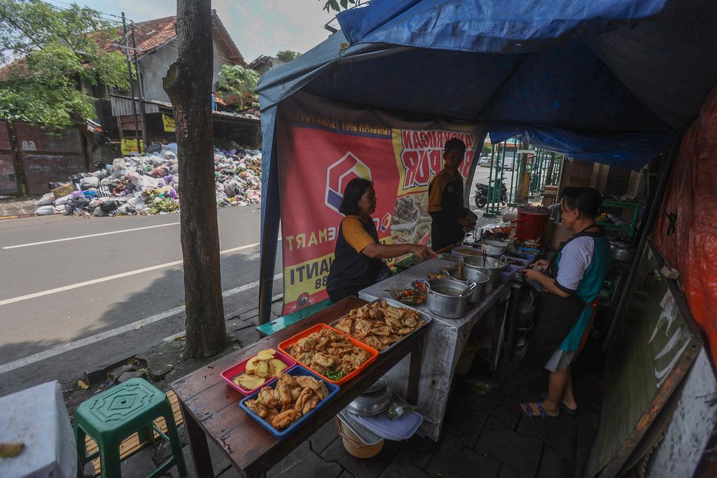Warga membeli makanan warung yang berada di seberang tumpukan sampah di kawasan Lempuyangan, Yogyakarta, Senin (10/5/2022). Tumpukan sampah terlihat di sejumlah lokasi di Yogyakarta pascapenutupan Tempat Pembuangan Sampah Terpadu (TPST) Piyungan oleh warga sejak 7 Mei 2022). 