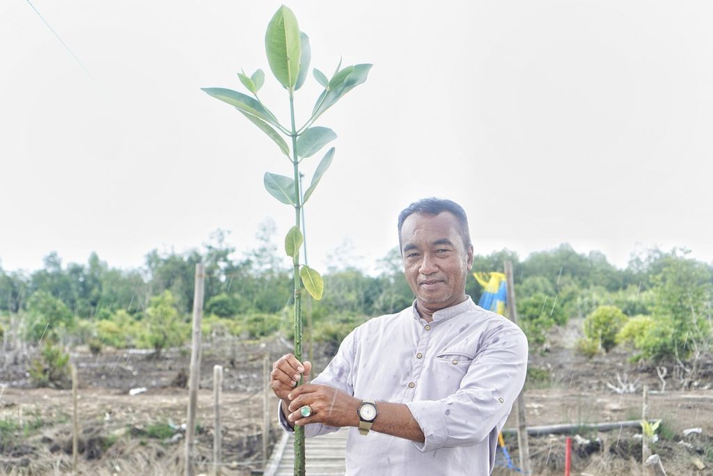 Ilham (56) berpose dengan salah satu bibit mangrove yang ia semai di kampungnya, Desa Muara Adang, Kecamatan Long Ikis, Kabupaten Paser, Kalimantan Timur, Rabu (15/2/2023).