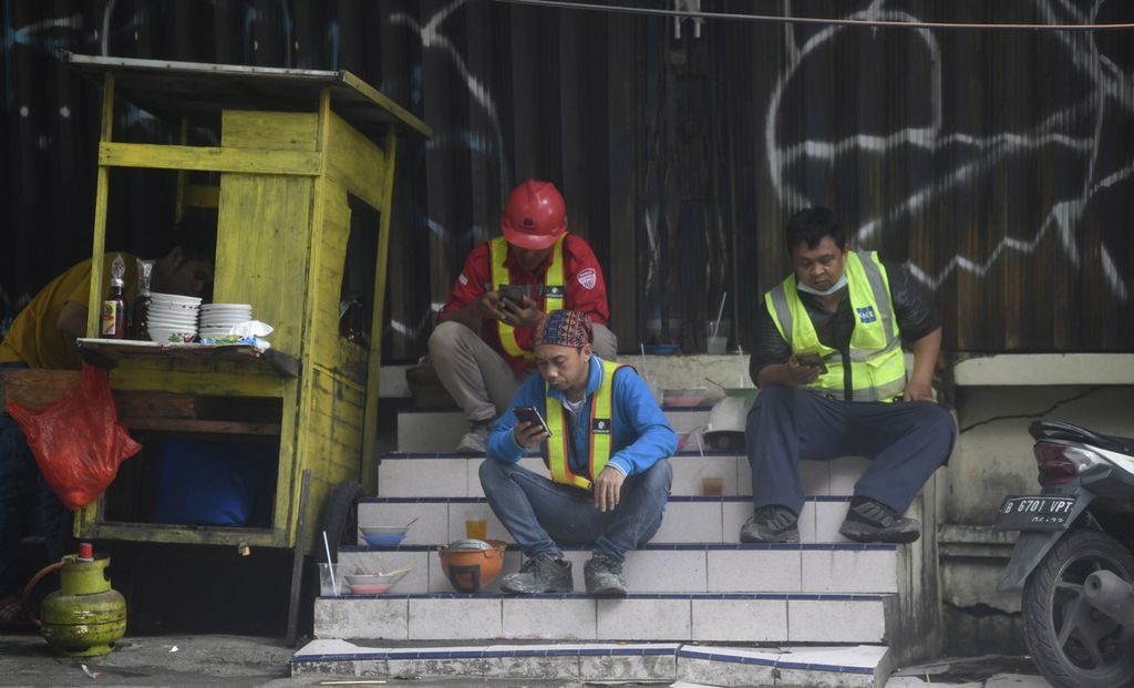 Sejumlah pekerja proyek sibuk melihat gawai masing-masing saat jam isitirahat makan siang di salah satu lokasi pembangunan gedung bertingkat di Jakarta, Kamis (17/2/2022). 