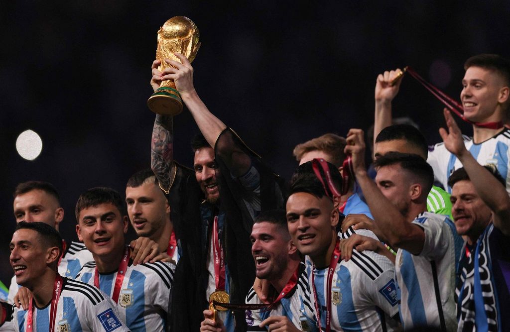 Kapten tim Argentina, Lionel Messi, mengangkat trofi juara Piala Dunia Qatar dalam acara penyerahan trofi setelah Argentina mengalahkan Perancis dalam pertandingan final di Stadion Lusail, Lusail, Qatar, Minggu (18/12/2022). 