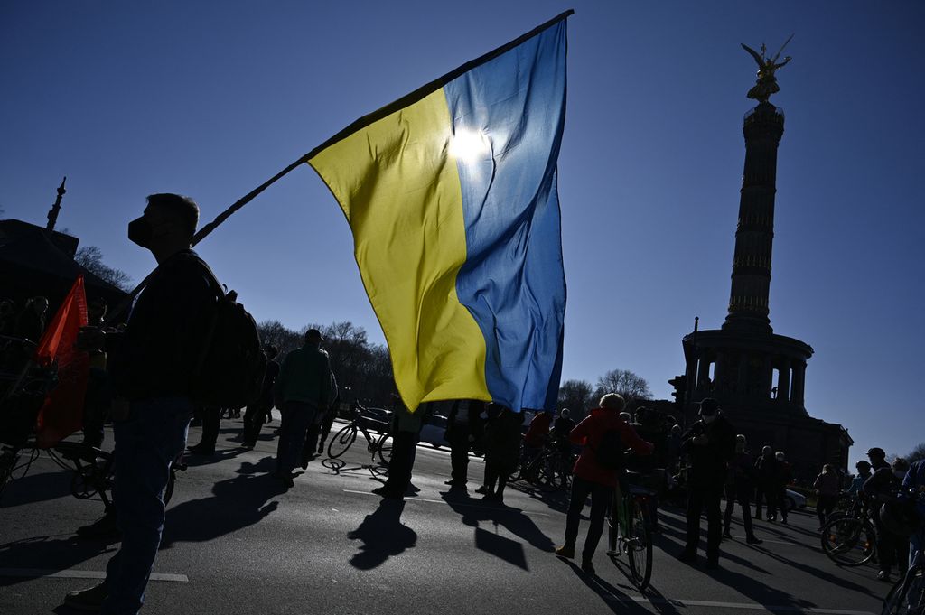 Seorang pengunjuk rasa memegang bendera Ukraina selama demonstrasi menentang invasi Rusia ke Ukraina, dekat Kolom Kemenangan di Berlin, Jerman, Minggu (13/3/2022). Aksi protes menentang invasi Rusia ke Ukraina bermunculan di berbagai negara.