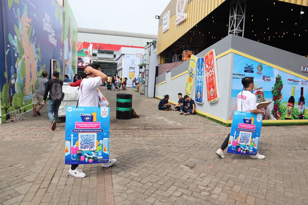 Pramuniaga berjalan dengan membawa papan promosi produk dompet digital untuk ditawarkan kepada pengunjung Jakarta Fair Kemayoran, Jakarta Pusat, Sabtu (18/6/2022).