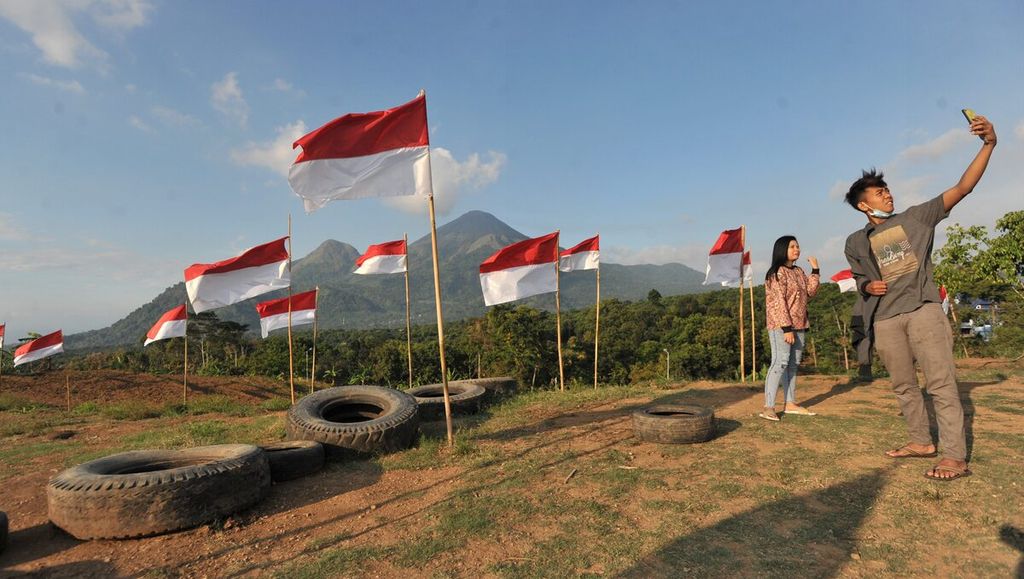 Wisawatan berfoto bersama bendera merah putih dengan latar belakang Gunung Penanggungan di objek wisata Potoek Suko, Kecamatan Trawas, Kabupaten Mojokerto, Jawa Timur, Sabtu (15/8/2020). 