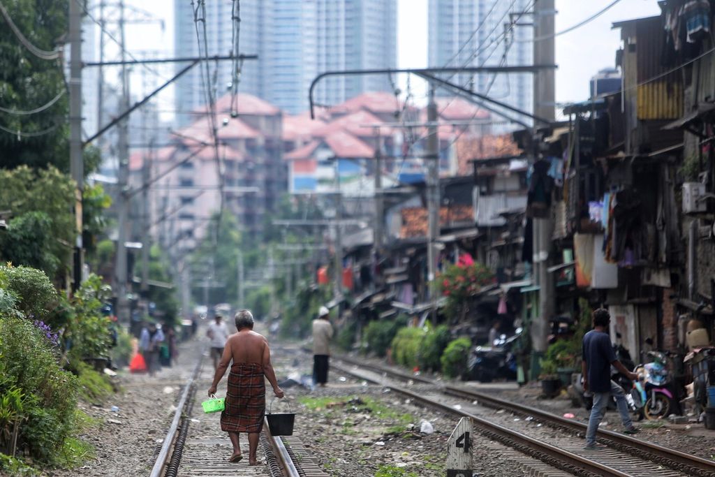 Warga menyusuri rel menuju tempat mandi umum di permukiman padat penduduk di tepi jalur KRL, Petamburan, Jakarta Pusat, Kamis (25/3/2021). Berdasarkan data Badan Pusat Statistik, tingkat kemiskinan Indonesia per September 2020 sebesar 10,19 persen atau 27,55 juta orang. 