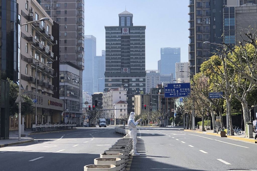 Pekerja dengan alat pelindung diri berdiri di tengah jalan yang sunyi saat penguncian wilayah di Distrik Jingan, Shanghai bagian barat, China, Senin (4/4/2022). China mengirim 10.000 pekerja kesehatan dari berbagai penjuru negeri untuk membendung laju penularan Covid-19 di Shanghai. 